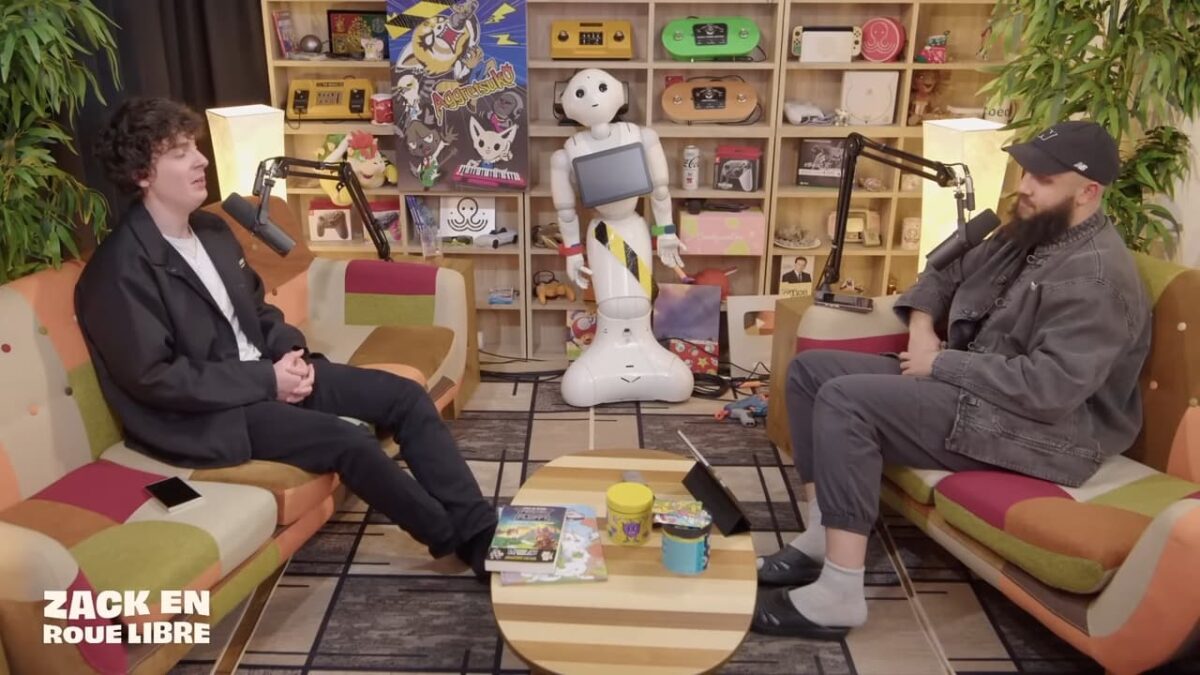 Frigiel en interview avec Zack Nani dans l’émission "Zack en Roue Libre". Les deux créateurs de contenu sont assis dans un décor coloré, entourés d’objets geeks et d’un robot humanoïde.