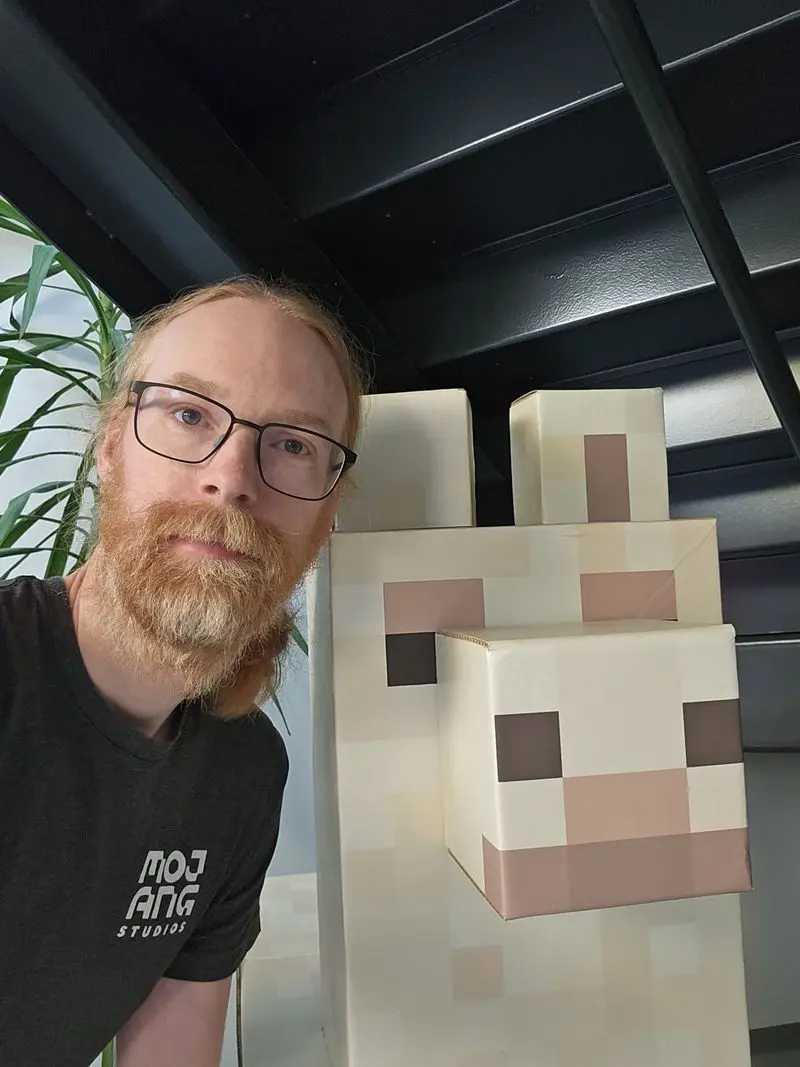 Jens Bergensten pose avec une statue de lama Minecraft grandeur nature dans les locaux de Mojang Studios.