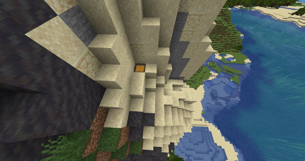 Coffre de trésor enfoui partiellement découvert sous le sable près de la mer dans Minecraft.