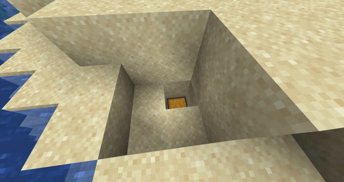 Coffre de trésor enfoui exposé dans une paroi sableuse en bord de mer dans Minecraft.