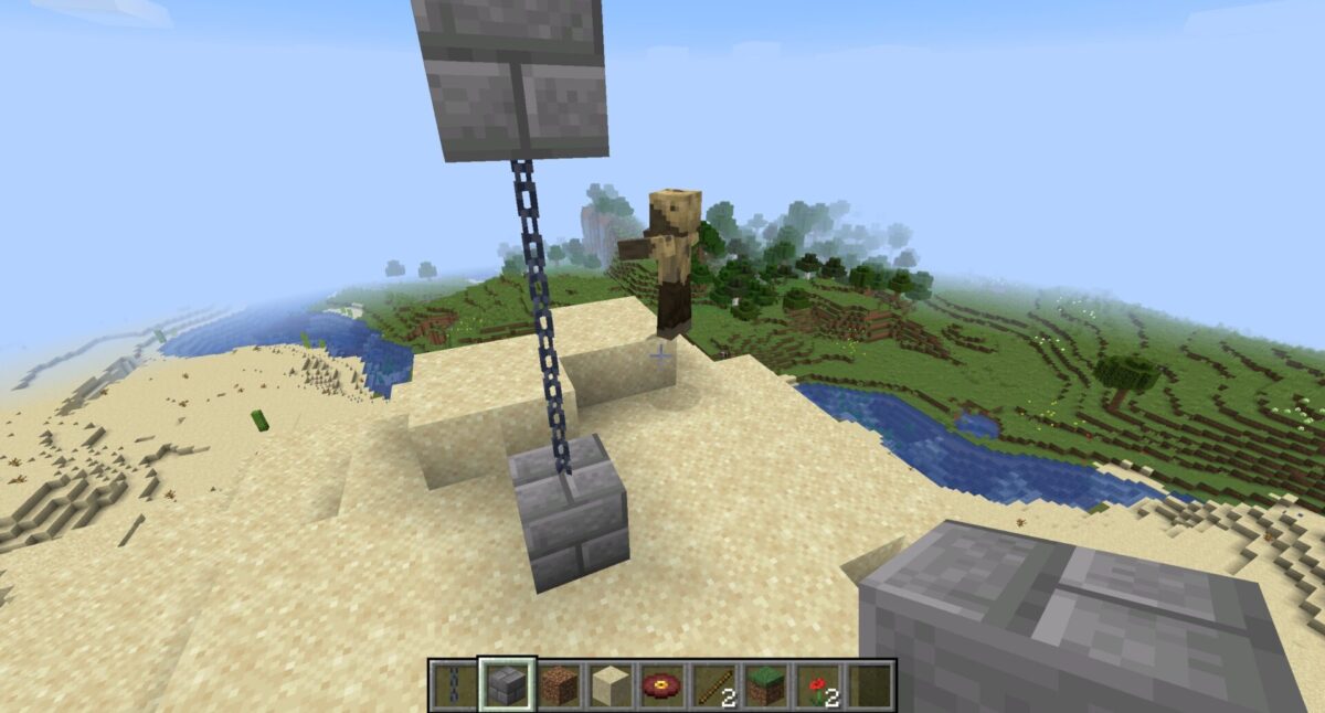 Deux blocs de pierre taillée reliés par une chaîne verticale dans Minecraft, sur un terrain sablonneux.