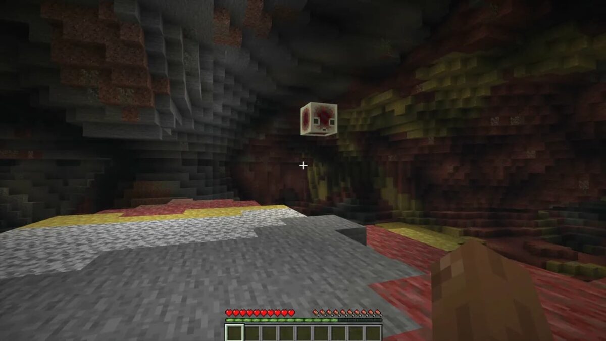 Un sulfur cube flottant dans une grotte de soufre, vu en première personne, avec un sol mêlant deepslate, soufre et cinabre