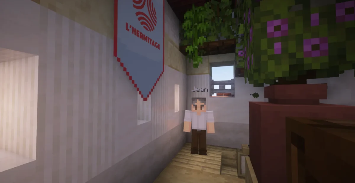 Le personnage de Jean près d’une bannière de L’Hermitage dans un intérieur de la Cité Solidaire